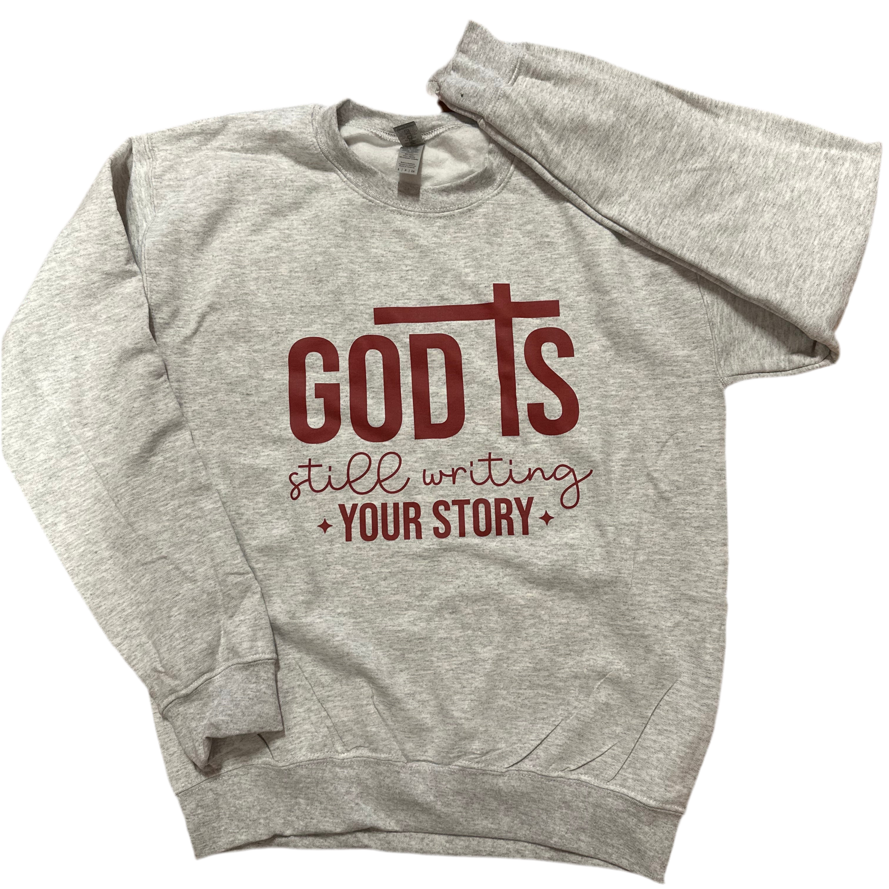 Gray hoodie with red text 'God is still writing your story' on a white background, faith based sweater, faith based clothing , God clothing